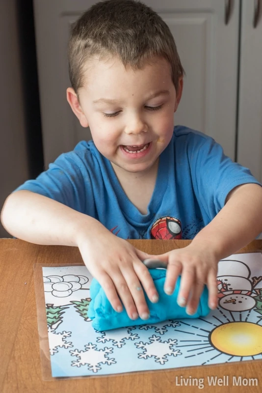 A young boy pressing playdough on top of a printable activity mat