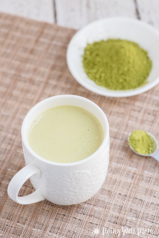 white mug with matcha green tea latte, white bowl with matcha powder and spoon 