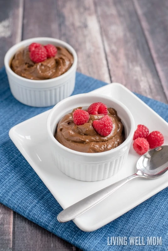 chocolate mousse topped with raspberries in white bowls on a blue placemat