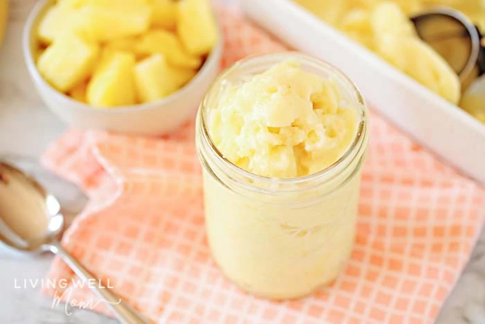 Pineapple ice cream on a table next to a bowl of fruit.