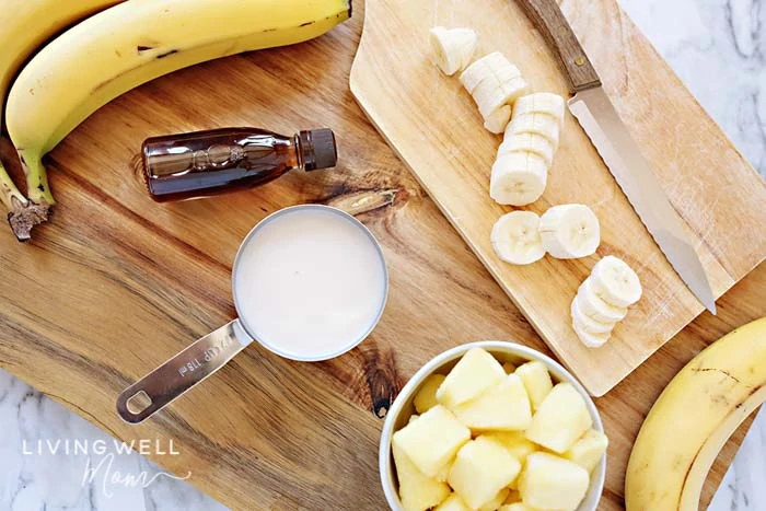 Dole whip ingredients including chunks of pineapple, slices of banana and a cup of coconut milk on a cutting board. 
