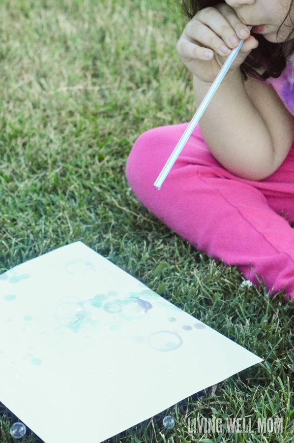 child blowing bubbles with straw onto paper for bubble activity