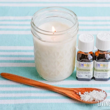 white citronella candle in mason jar with brown wood spoon and essential oil bottles