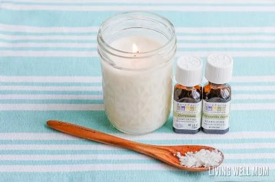 white citronella candle in mason jar with brown wood spoon and essential oil bottles 