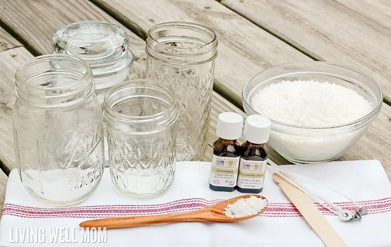 four empty glass jelly and mason jars next to ingredients for DIY candle-making