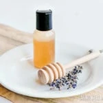 homemade honey face wash in a small bottle on a white plate with lavender flowers and honey scoop