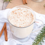 homemade vegan eggnog in a glass with cinnamon sticks and pine branches