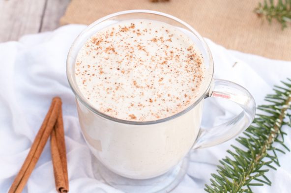 homemade vegan eggnog in a glass with cinnamon sticks and pine branches