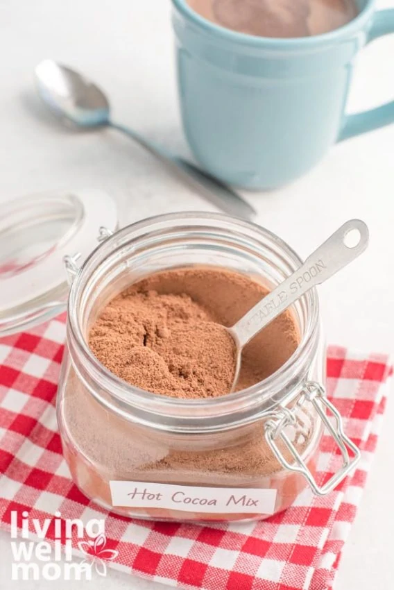 homemade cocoa mix in glass container with red checkered napkin and blue mug