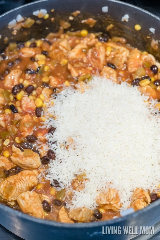 White rice being poured into ingredients for one-pot enchilada casserole dish.