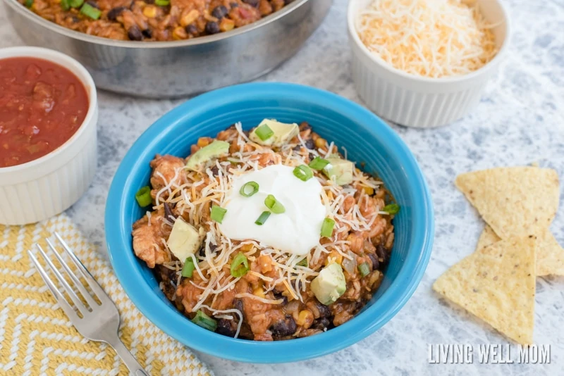 A blue bowl of Mexican turkey enchilada casserole, topped with sour cream and green onions, with chips nearby. 