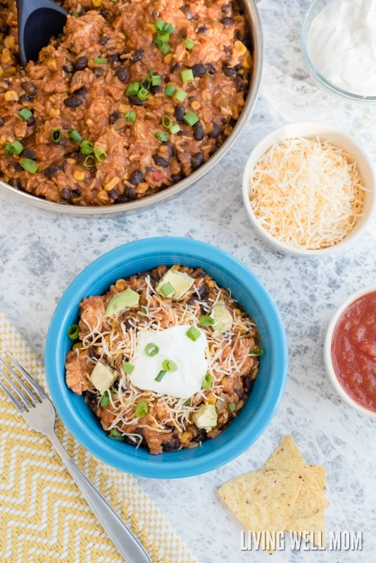 A pan full of Mexican casserole with a bowl of it nearby, with cheese, sour cream and salsa for topping. 