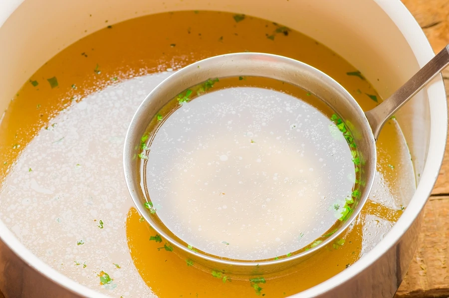 ladle of bone broth in a white bowl