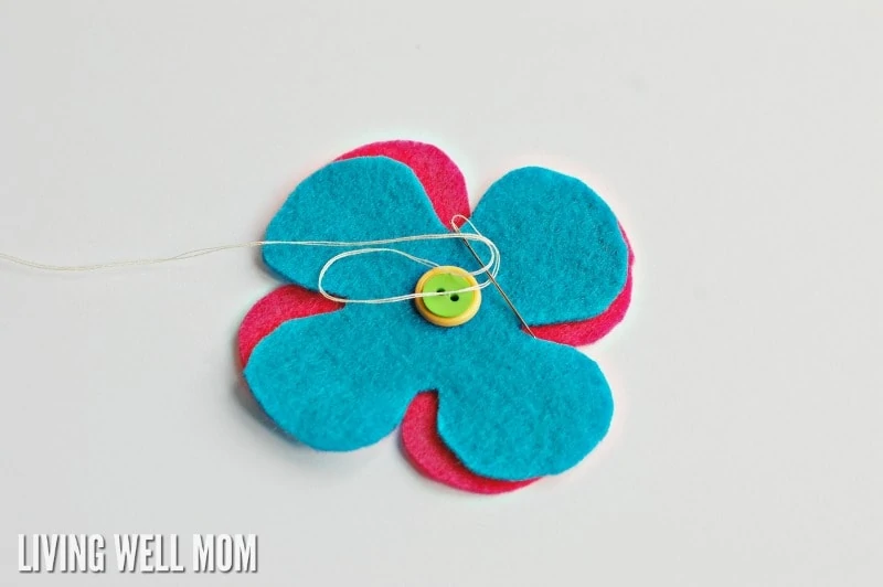 sewing together blue and pink felt flowers with buttons and thread