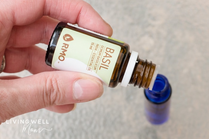 drops of basil essential oil being put into a blue roller bottle