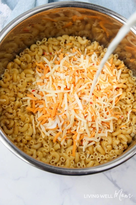 Shredded cheese and milk being added to cooked gluten-free pasta. 