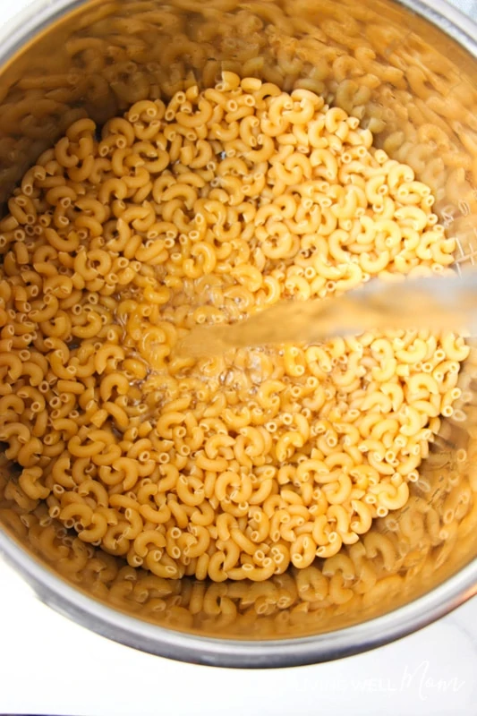 Gluten-free macaroni in a sauce pan being filled with water. 