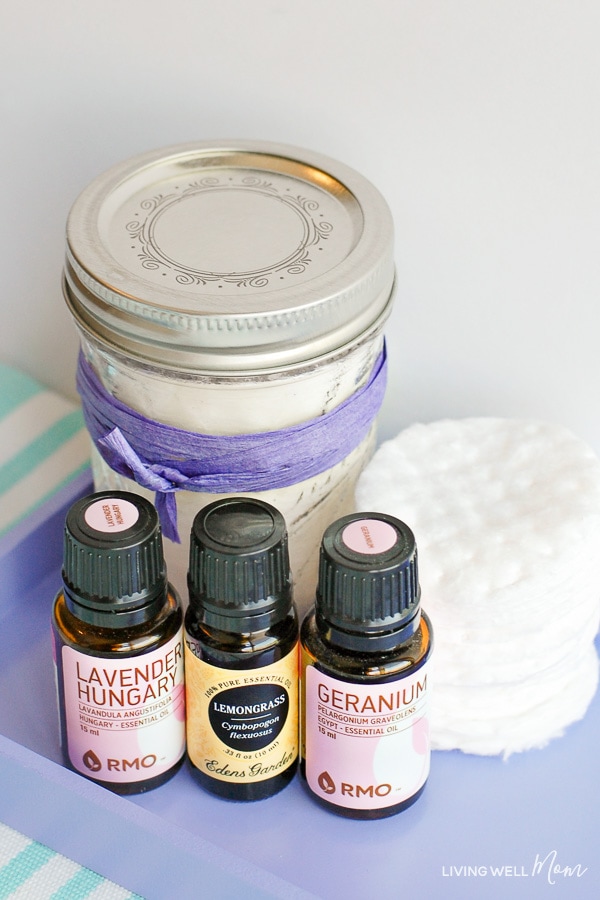 A container of homemade facial toner pads and bottles of lavender, lemongrass and geranium essential oil. 