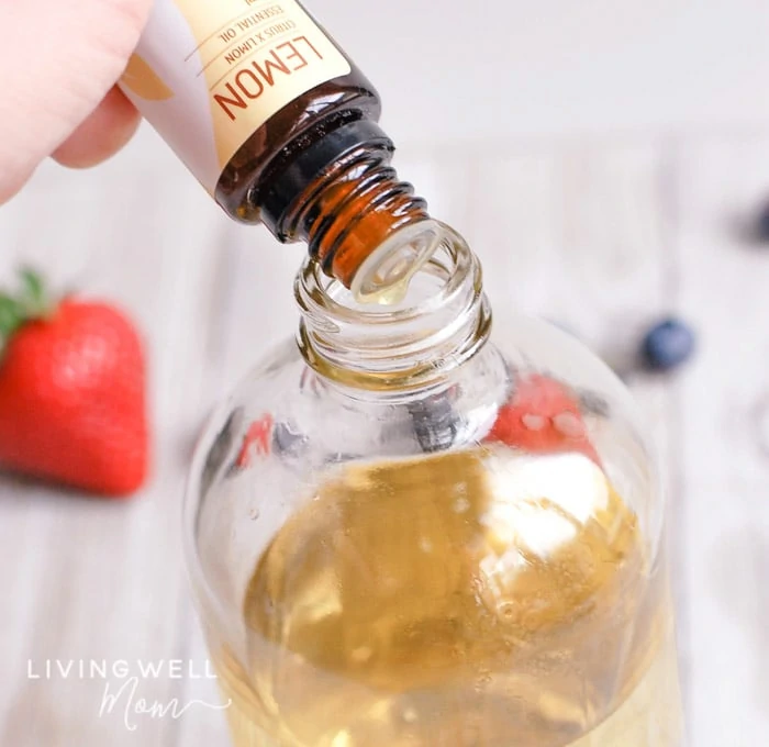 Lemon essential oil being dropped into bottle of fruit and vegetable wash. 