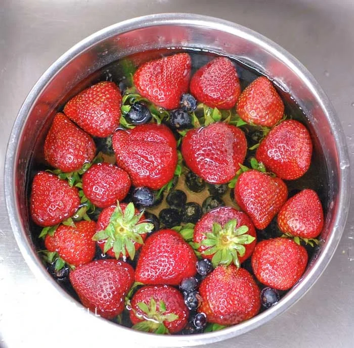 Strawberries and blueberries in a bowl full of homemade fruit and vegetable soak