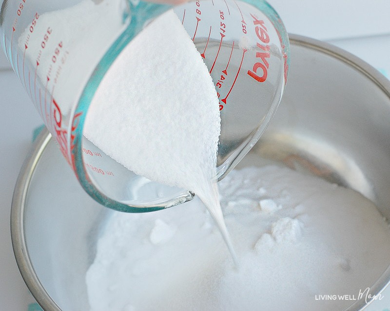 A measuring cup of sea salt being poured into a glass bowl of baking soda. 