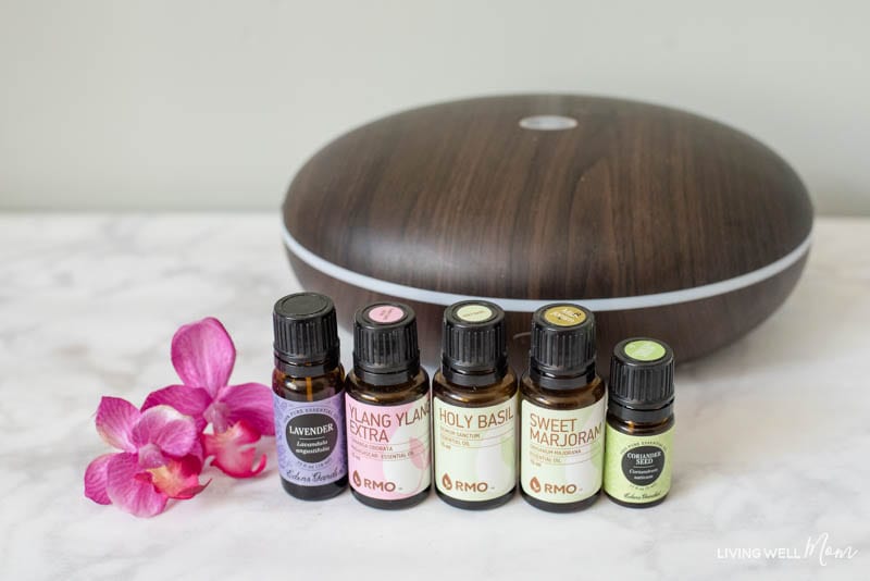 Lavender, ylang ylang, holy basil, sweet marjoram and coriander seed oil near a diffuser. 