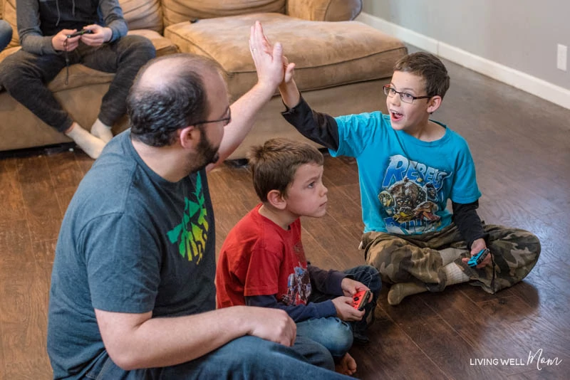 a father and a son high-fiving over a boy concentrating on a game 