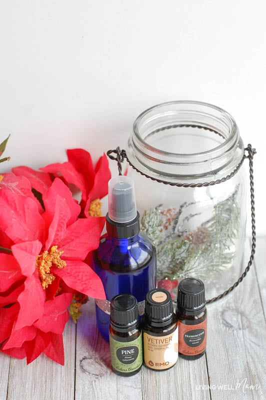 a spray bottle, some essential oils, a glass jar, and some red flowers 