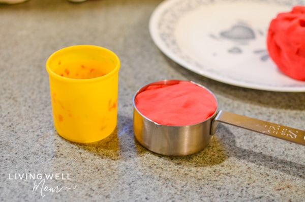 A scoop of red colored DIY playdpugh in a measuring cup.