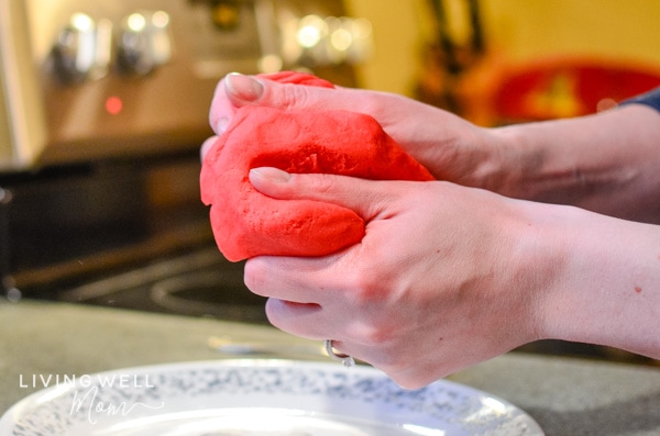 Red, homemade playdough being squeezed in a person's hands. 