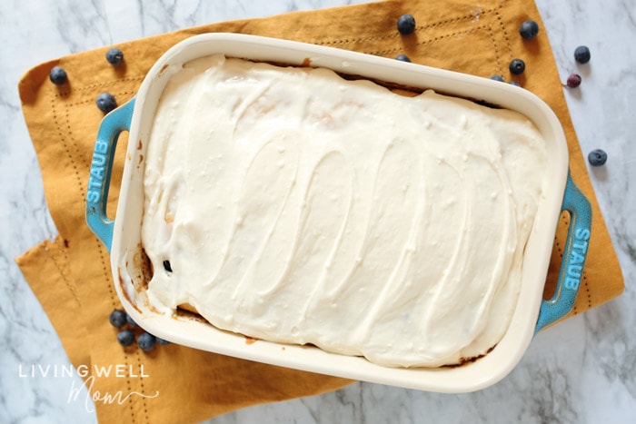 Cream cheese icing spread over a blueberry dump cake in a baking pan.