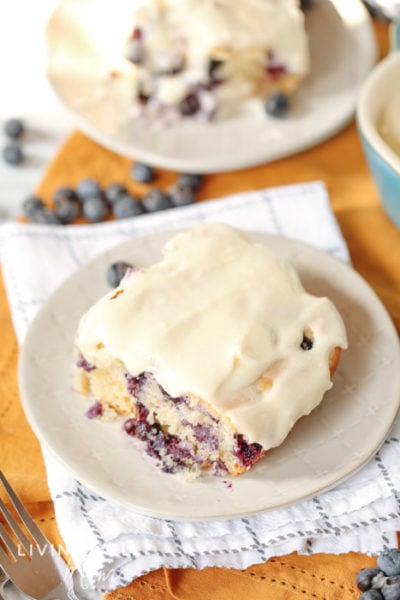 Blueberry cake with cream cheese icing on plates, with blueberries scattered on the table. 