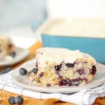 a piece of blueberry dump cake with cream icing on a plate
