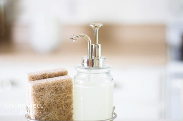 Lavender essential oil dish soap in a dispenser besides two natural sponges.