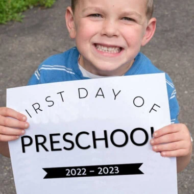 smiling boy holding first day of preschool 2022 sign