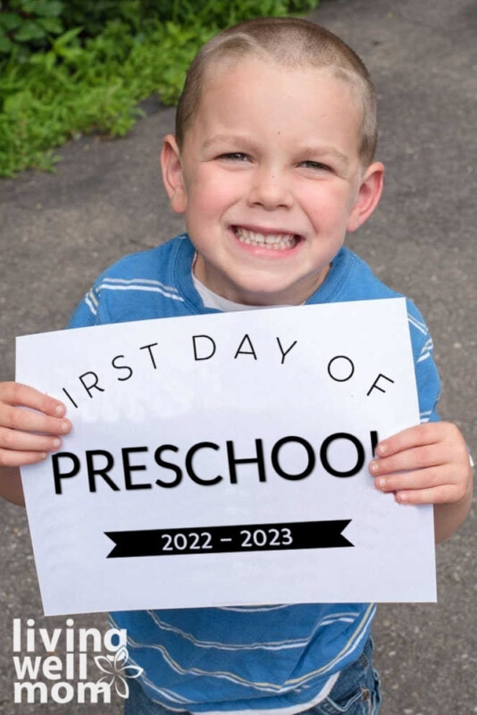 smiling boy holding first day of preschool 2022 sign