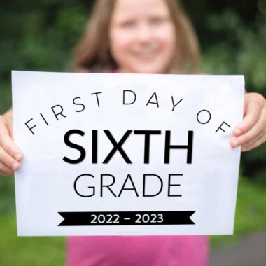 girl wearing pink shirt holding up printed first day of sixth grade 2022 sign