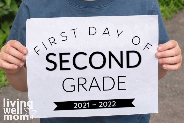 child holding first day of second grade printed sign