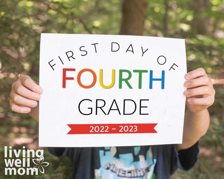boy holding colorful first day of fourth grade sign in woods