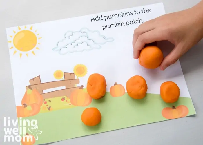 orange balls of playdough being added as pumpkins on activity mat
