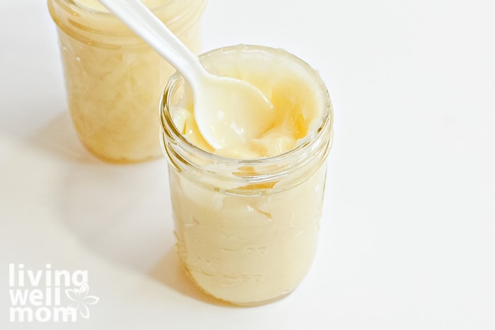 a small mason jar of DIY lotion being scooped up in a plastic spoon