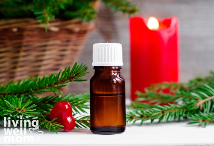 a bottle oil essential oil sitting in front of a red candle and a twig of garland