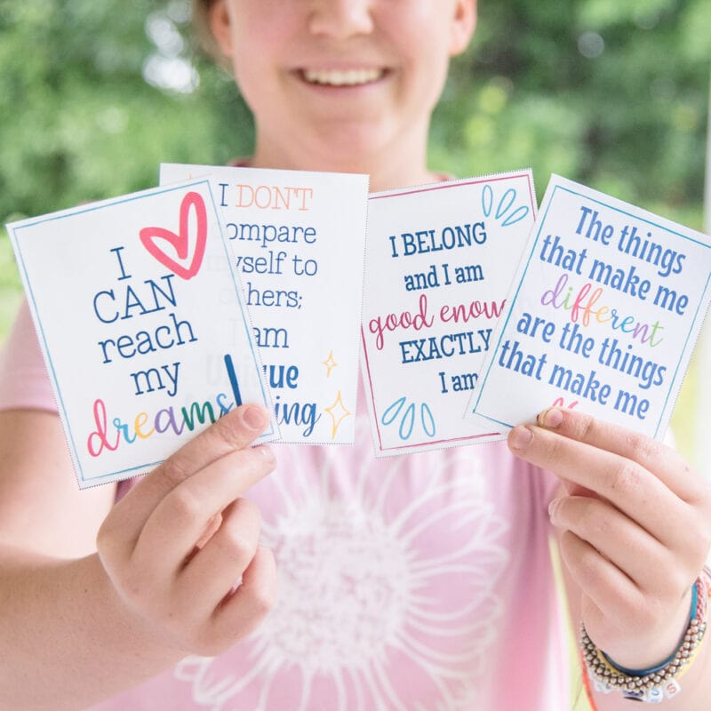 teenager girl holding positive affirmation cards with green forest background