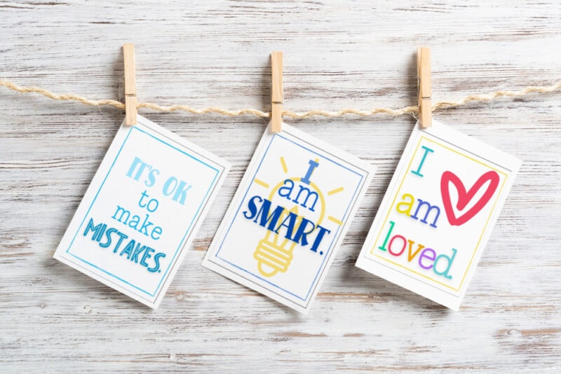 positive affirmation cards for children hanging from clothespins on wood background