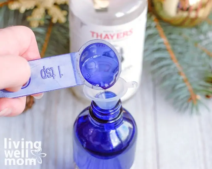 teaspoon of ingredients being added into blue glass bottle