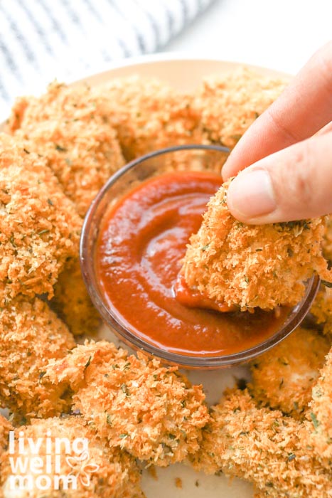 fingers holding oven-baked chicken nugget dipping into red ketchup sauce