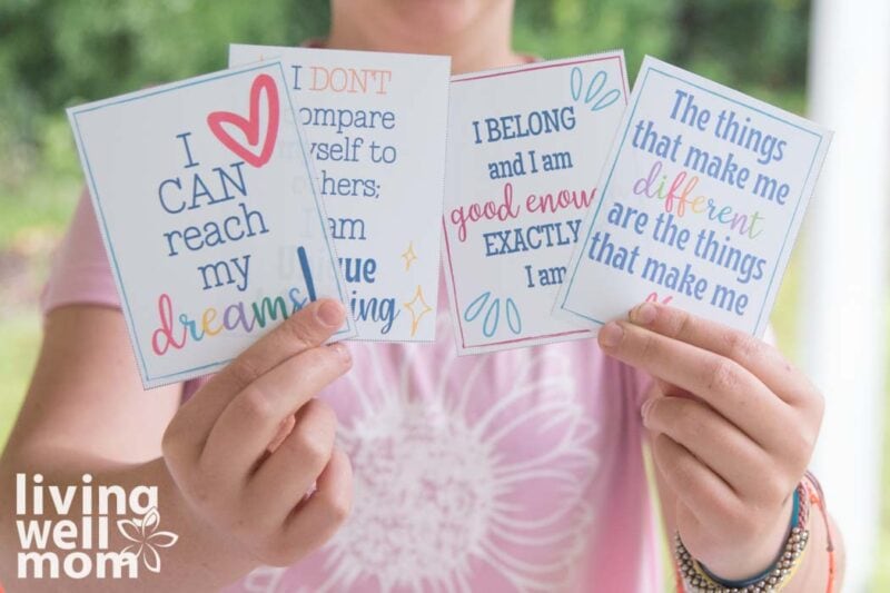 teenage girl holding four colorful printable affirmations in her hands. 