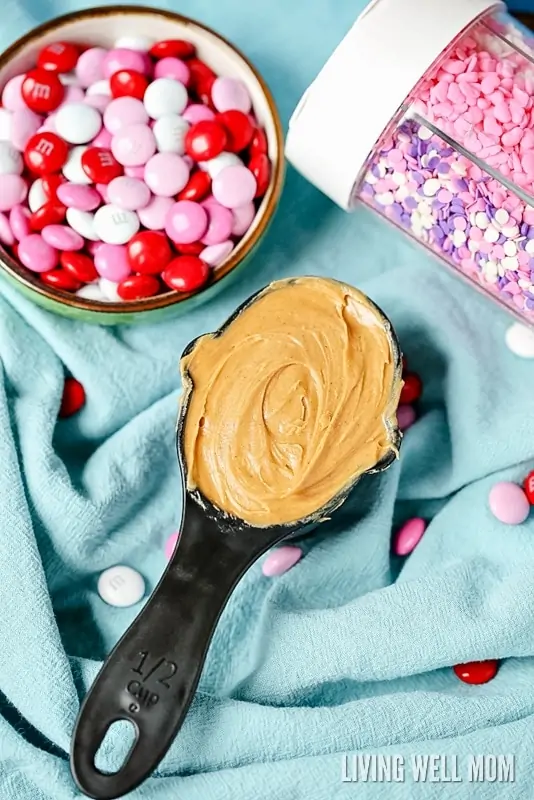 a measuring cup of peanut butter next to pink and red sprinkles and m&m candy