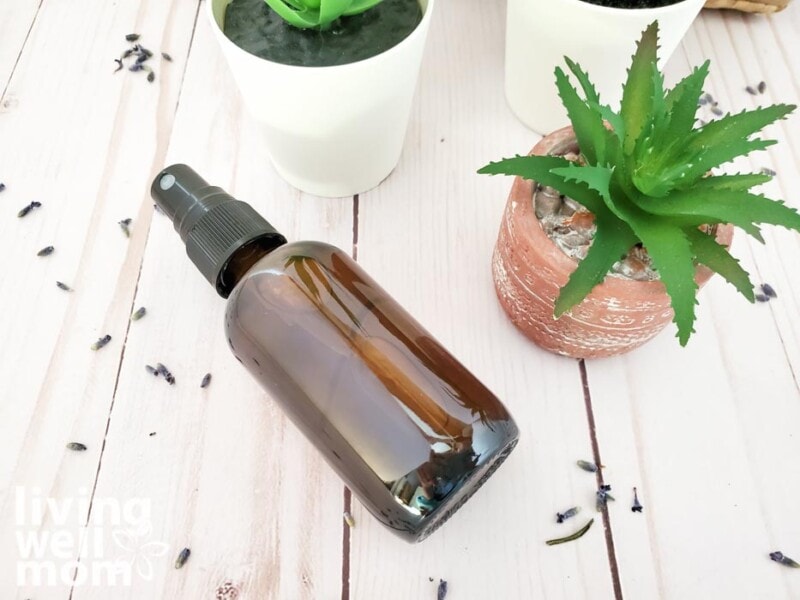 bottle of essential oil spray on a wooden surface surrounded by faux plants