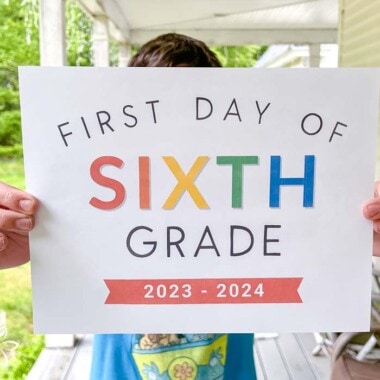 boy with blue shirt holding rainbow colored paper that says first day of sixth grade 2023-2024